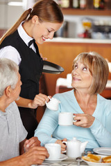 Kellnerin schenkt Seniorin Milch in den Kaffee