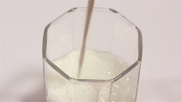 Milk flowing in  transparent cup. Close up