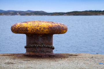 Old rusted yellow mooring bollard with chain on pier
