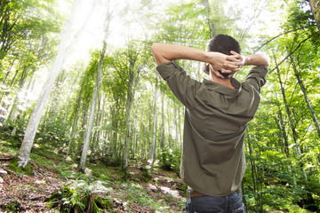 young man enjoying sunlight in a green summer forest