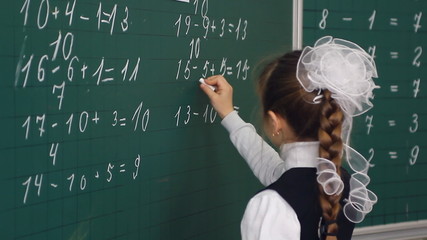 schoolgirl writing on blackboard in classroom - Powered by Adobe