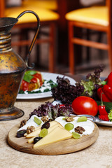 Cheese and fruits wooden platter with vegetables and herbs in th