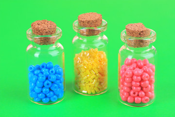 Different colorful beads in bottles on green background