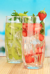 Glasses of fruit drinks with ice cubes on blue background