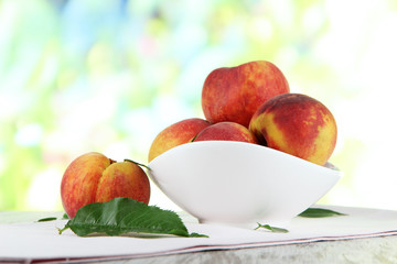 Peaches in plate on napkin on wooden table on nature background