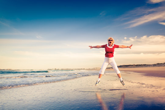 Senior woman enjoying beach holiday jumping in air