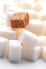 one brown sugar lump in front of lots of white sugar cubes backl