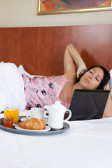 Obraz na płótnie Canvas Frau wacht auf mit Hotelfrühstück und Laptop