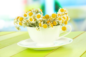 Bouquet of chamomile flowers in cup, on bright background
