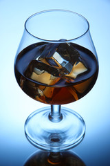 Brandy glass with ice on blue background