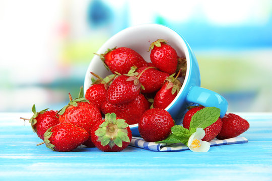 Ripe sweet strawberries in cup on blue wooden table