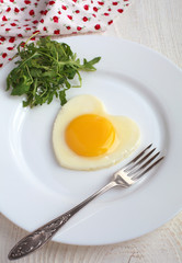 Fried egg in a heart shape with Rocket anf fork in white plate o