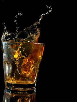 Glass of whiskey with splash, isolated on black