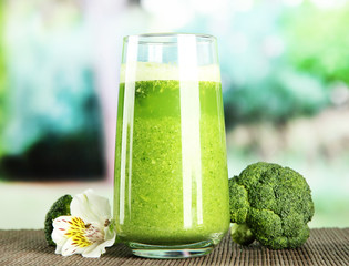 Glass of broccoli juice, on bamboo mat, on green background