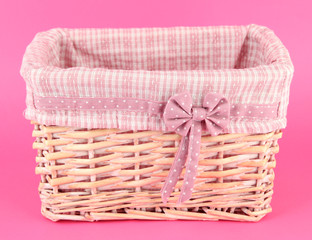 Fototapeta na wymiar Wicket basket with pink fabric and bow, on color background
