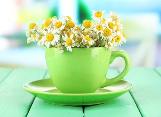 Bouquet of chamomile flowers in cup, on bright background