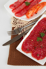 Tasty salami on plates on  napkin isolated on white