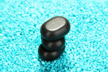 Fototapeta na wymiar Black stones on blue crystals of sea salt background