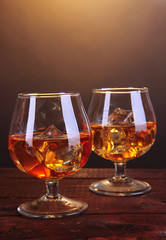 Brandy glasses with ice on wooden table on brown background