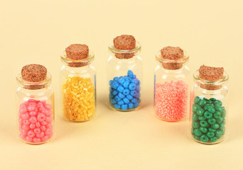 Different colorful beads in bottles on beige background