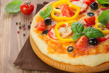 Pizza with ham, tomato and olives and vegetables on wooden table