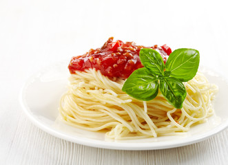 Spaghetti bolognese and green basil leaf on white plate