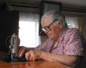 elderly woman in glasses, sewing on sewing machine