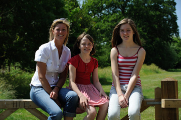 Fototapeta premium Portrait of a woman and two girls sitting on a fence