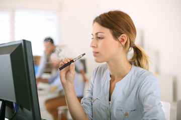 Girl smoking with electronic cigarette in office