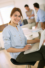 Cheerful girl in office sitting on chair with laptop