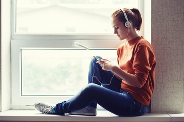 Girl sits on window sill and listens to music