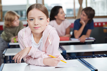 Schoolgirl Leaning On Desk With Students In Background