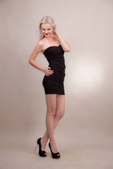Beautiful girl  in a short black dress on a gray background.