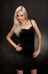 Fototapeta premium Beautiful girl in a short black dress on a black background.