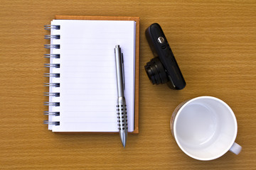 Note book and pen and coffee cup and camera. On the floor of the