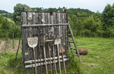 Used farm hand implements on wooden shed wall background