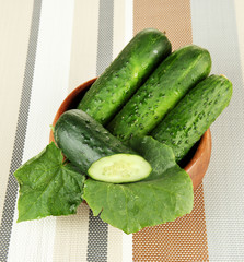 Tasty green cucumbers in wooden bowl, on bright background