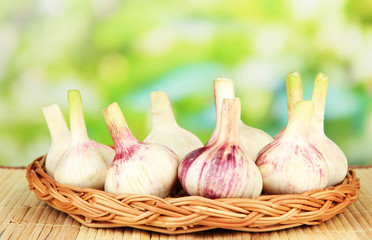 Fresh garlic on wicker mat, on bright background