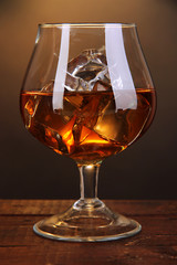 Brandy glass with ice on wooden table on brown background