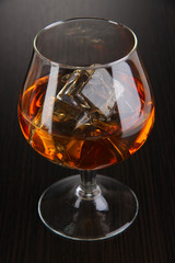 Brandy glass with ice on wooden background