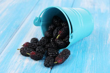 Ripe mulberries in bucket on wooden background