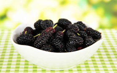 Ripe mulberries in bowl on table on bright background