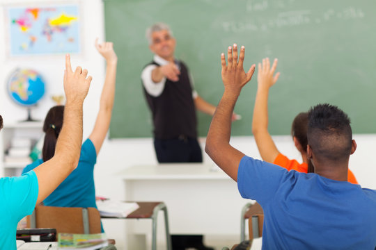 high school students with hands up in classroom