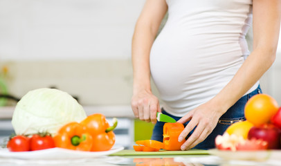 Obraz na płótnie Canvas Close up pregnant woman with knife on kitchen cuts vegetables