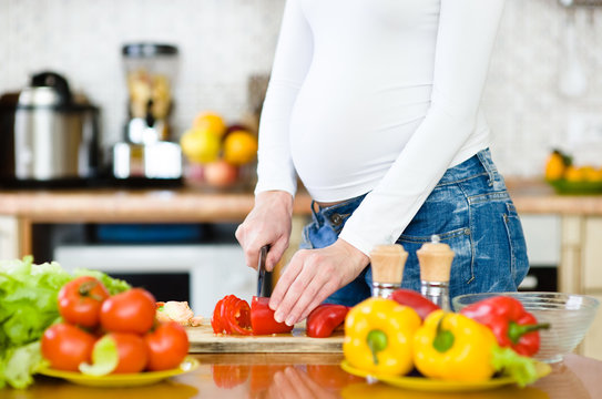 Close up pregnant woman with knife on kitchen cuts vegetables