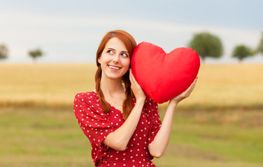 Redhead girl with toy heart at meadow near wheat field