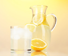 Lemonade in pitcher and glass on yellow background