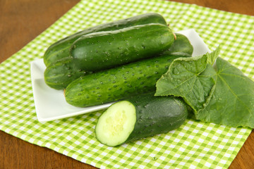 Tasty green cucumbers on color napkin, on wooden background
