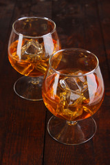 Brandy glasses with ice on wooden background