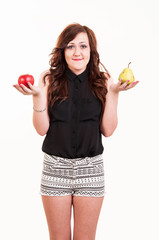 Young woman comparing an apple and a pear, trying to decide whic
